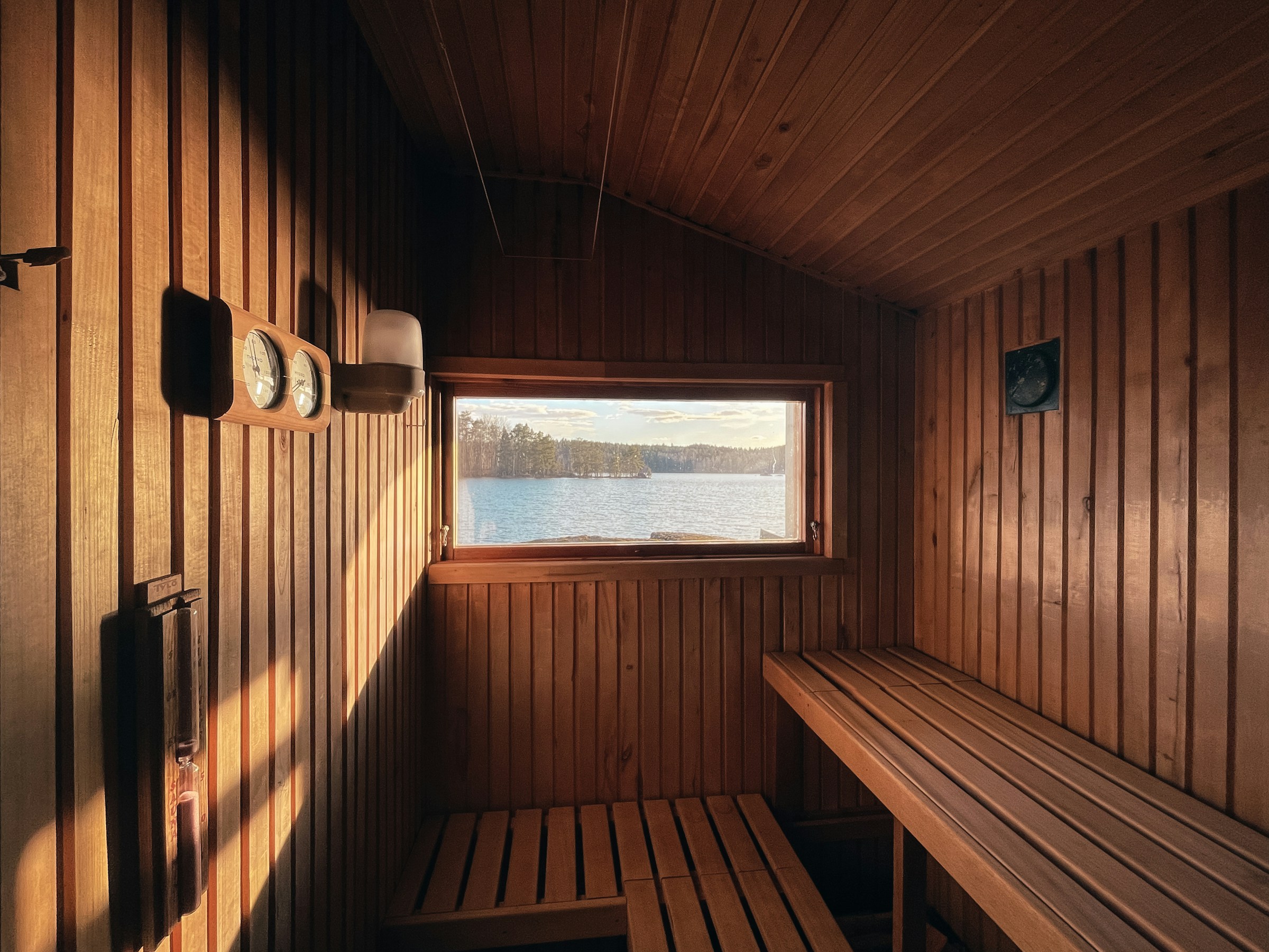 Warm wooden sauna with tiered benches and a window overlooking a lake